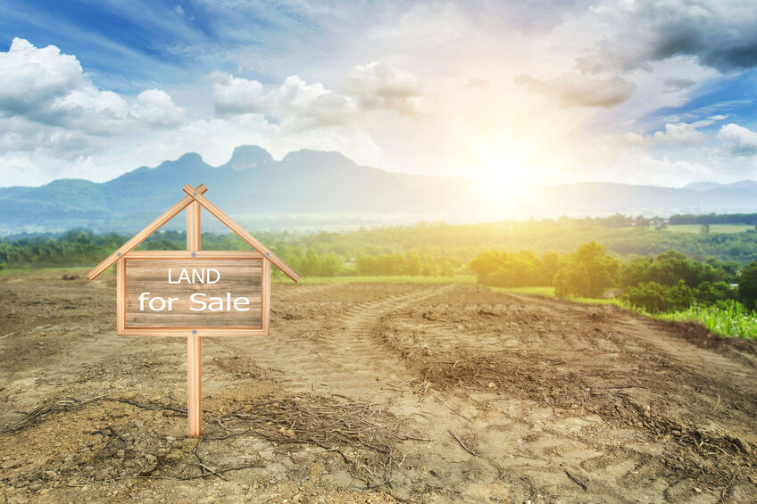 “Land for sale” sign on empty plot of land with blue sky and sun setting in the background