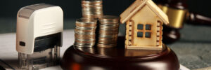 A row of coins on a small house model and a law auction hammer