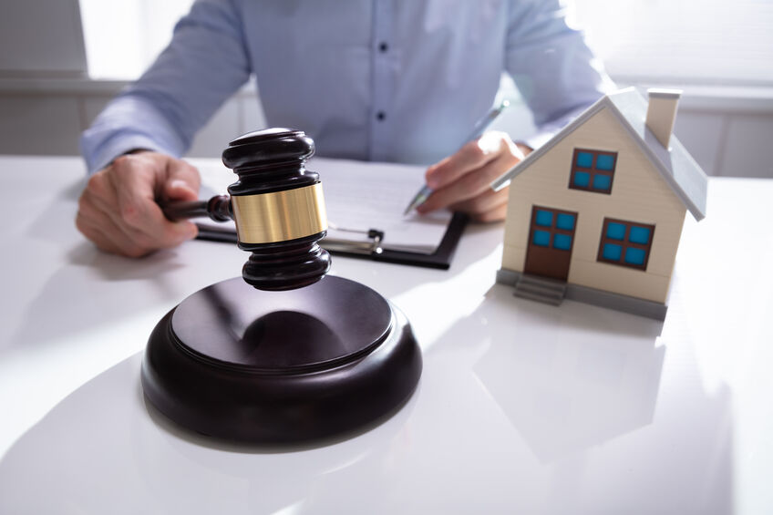 Judge Holding Gavel With House Model At Desk